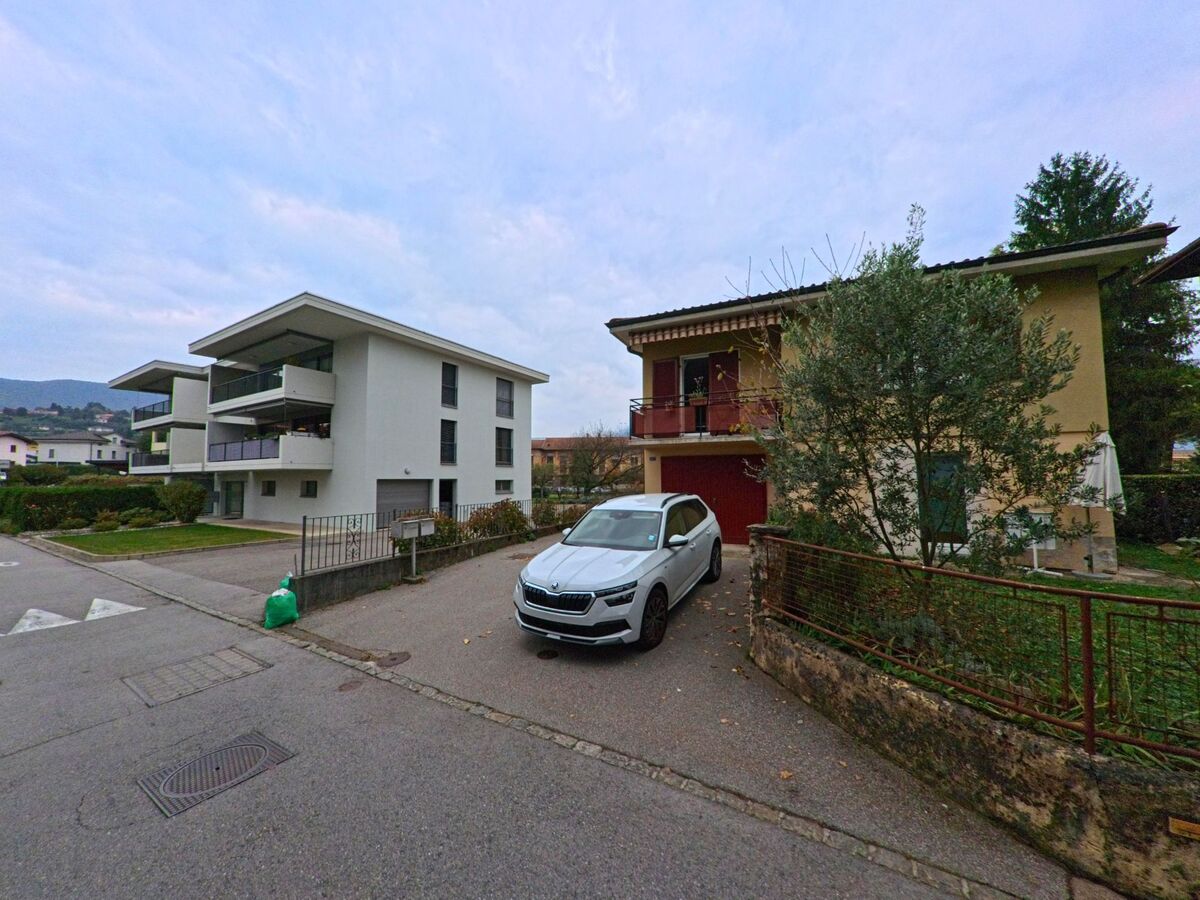 In Stabio (6854, Kanton Tessin) stehen moderne Mehrfamilienhaeuser und ein traditionelles Wohnhaus mit Balkon nebeneinander an einer ruhigen Quartierstrasse.