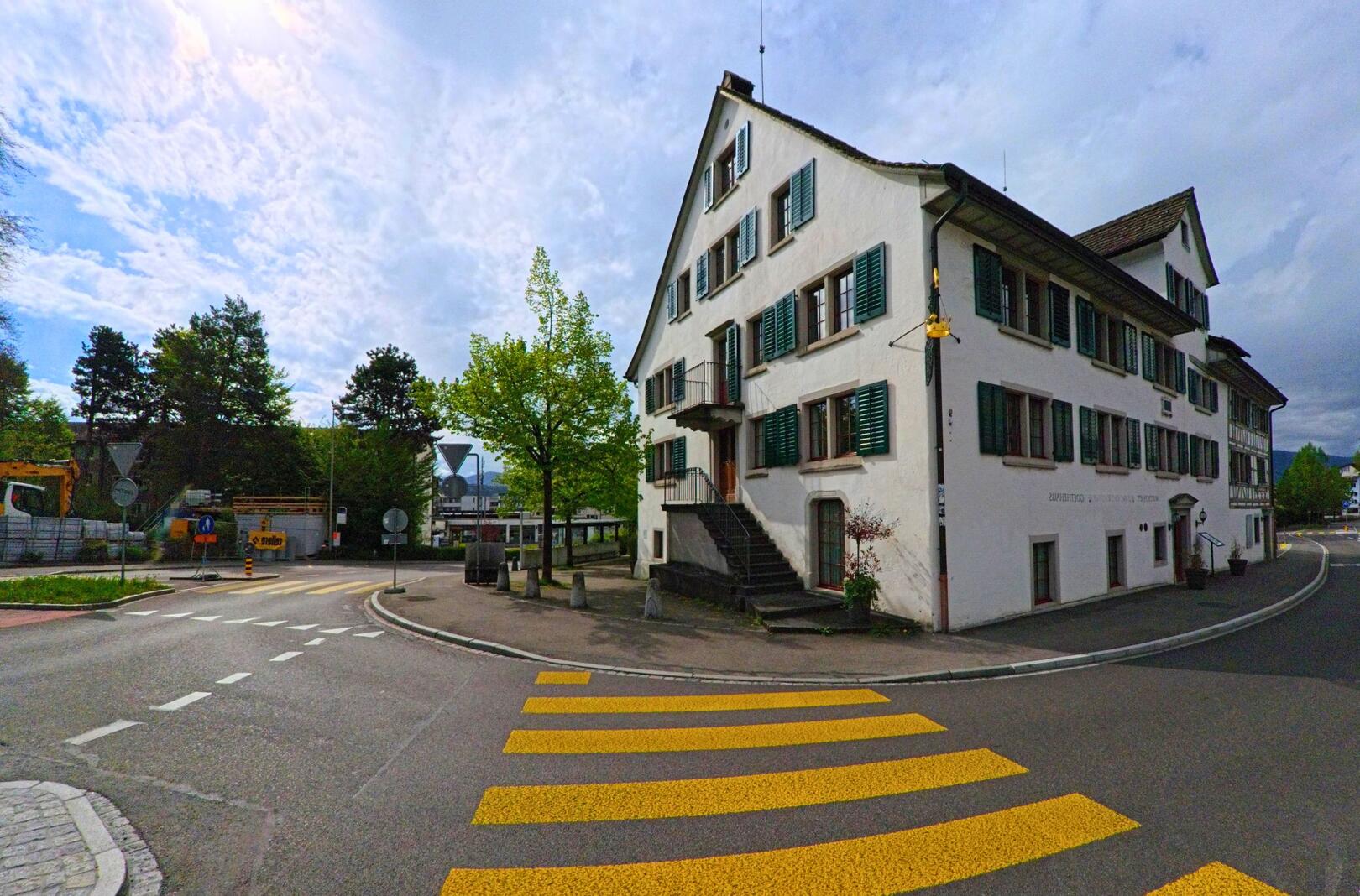 In Stäfa (8712, Kanton Zürich) steht das traditionsreiche Gasthaus „Alte Krone“ an einer Strassenkreuzung mit markantem Zebrastreifen und Blick auf das Quartier.