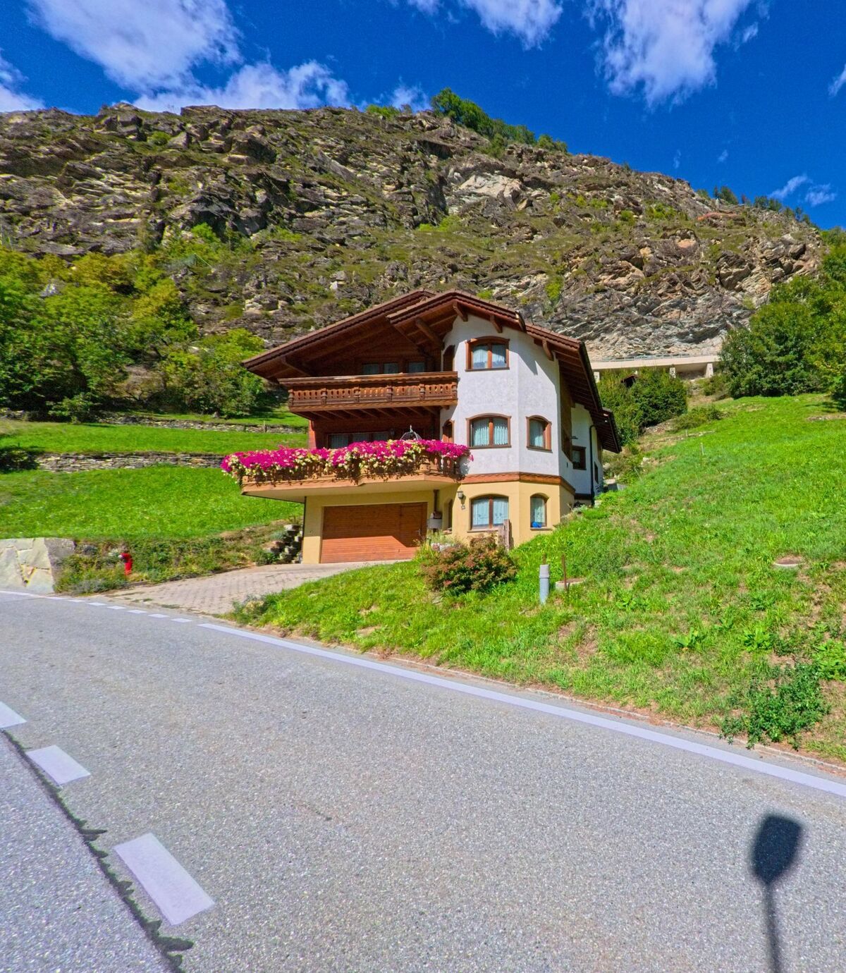 Ein Einfamilienhaus mit Blumenbalkon steht in Stalden (3922, Kanton Wallis) direkt am steilen Hang unterhalb einer markanten Felswand.