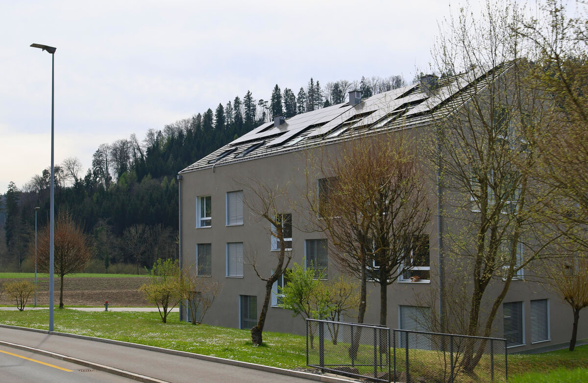 In Stallikon (8143, Kanton Zürich) grenzen moderne Wohnbauten mit Solarpanelen auf dem Dach direkt an offene Felder und bewaldete Hügel.