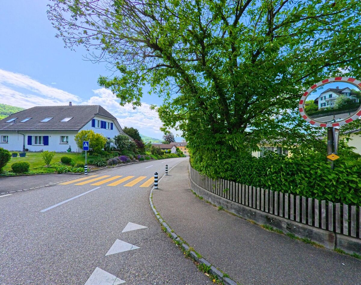 In Starrkirch-Wil (4656, Kanton Solothurn) liegt ein Fussgaengeruebergang in einer ruhigen Wohngegend, eingerahmt von Baeumen, Hecken und einem Verkehrsspiegel.