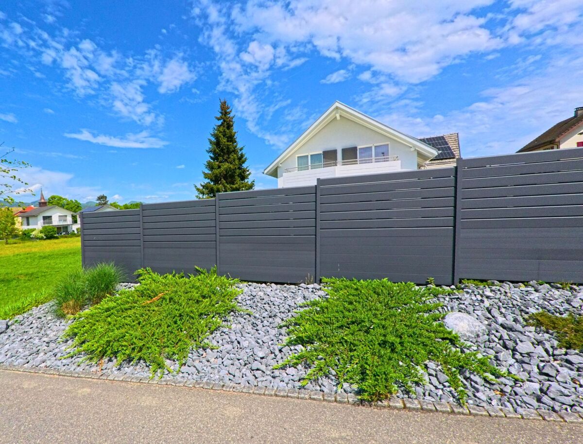 In Starrkirch-Wil (4656, Kanton Solothurn) verläuft eine ruhige Strasse an modernen Einfamilienhaeusern vorbei, gesaeumt von einem Kiesbeet mit Sichtschutzzaun.