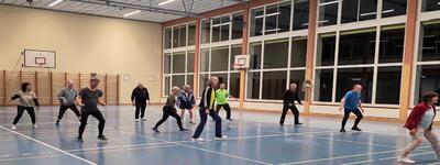 In Bern (3011, Kanton Bern) trainiert eine Gruppe von Erwachsenen gemeinsam in einer Turnhalle und fuehrt Bewegungsuebungen aus.