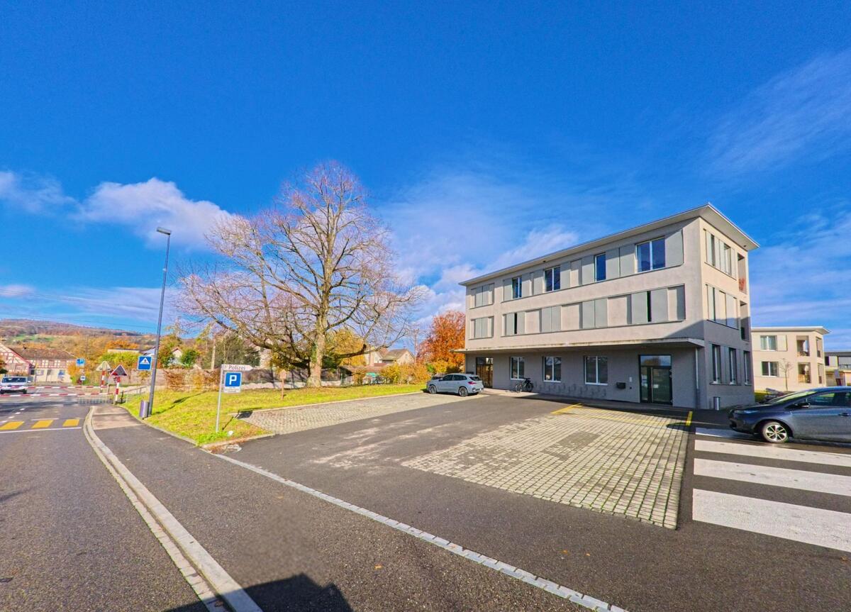 Neben einem offenen Parkplatz mit Fussgängerstreifen steht in Steckborn (8266, Kanton Thurgau) ein sachliches Verwaltungsgebäude vor kahlen Bäumen und blauem Himmel.