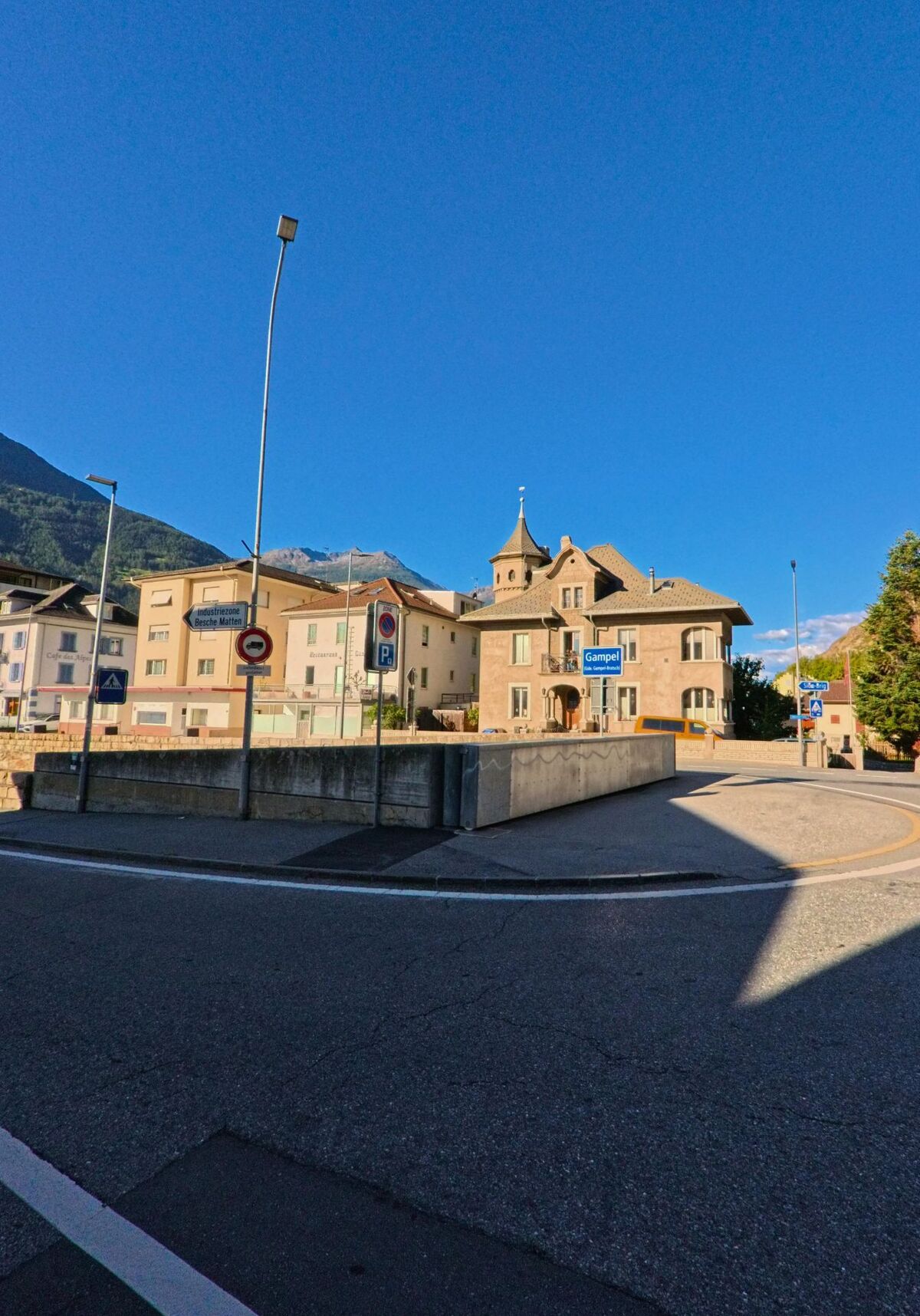 An einer Strassenkreuzung in Steg-Hohtenn (3945, Kanton Wallis) steht ein markantes Haus mit Turmfassade vor der Kulisse der Berge.
