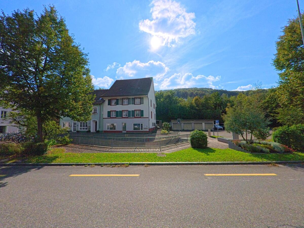 Vor bewaldeten Huegeln steht in Stein (4332, Kanton Aargau) ein Wohnhaus mit gruener Fassade, umgeben von kleinen Gartenflaechen und einem angrenzenden Parkplatz.