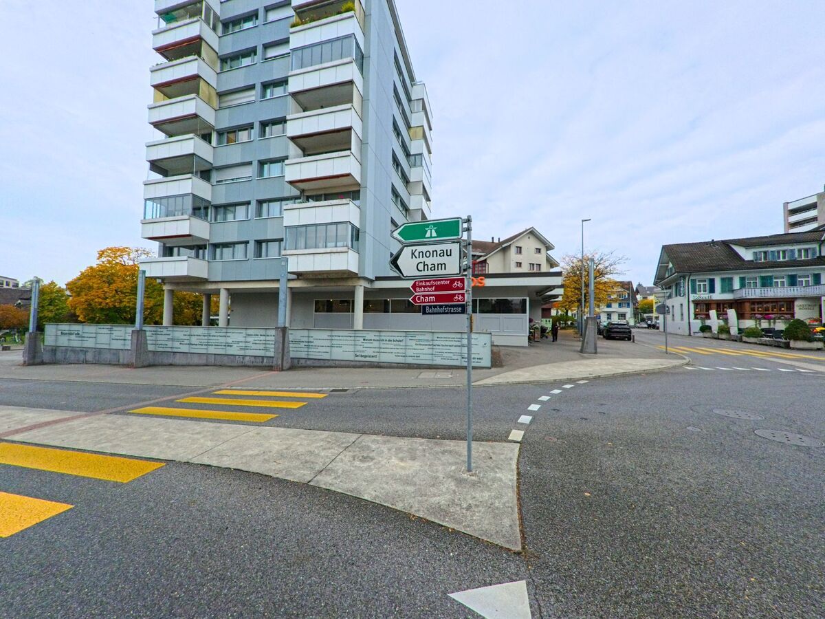 An einer übersichtlichen Kreuzung mit Wegweisern zeigt sich das Ortsgebiet von Steinhausen (6312, Kanton Zug).