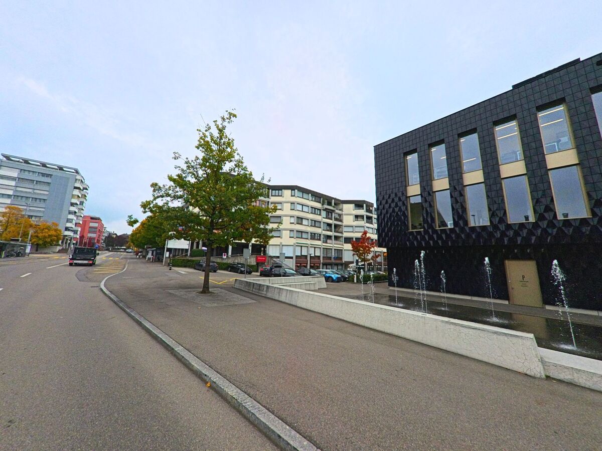 Ein Wasserbecken begleitet den Gehbereich vor zeitgemässen Gebäuden in Steinhausen (6312, Kanton Zug).