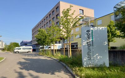 An einer Zufahrt in Zürich (8051, Kanton Zürich) steht das moderne Gebäude der Stiftung Altried mit begrüntem Vorplatz und beschrifteter Stele im Vordergrund.