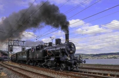 Eine historische Dampflok fährt auf den Gleisen der Stiftung Bahnpark in Brugg (5200, Kanton Aargau) und stösst dichten Rauch in den Himmel.