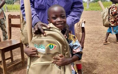 Ein Kind haelt in Andwil 9204 im Kanton St. Gallen einen Schulrucksack waehrend einer Hilfsaktion im Freien in den Haenden.