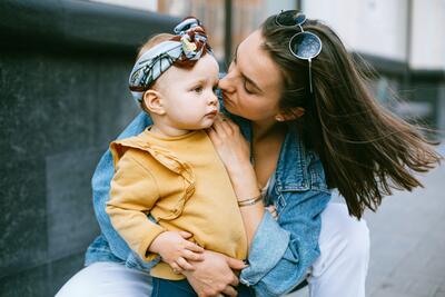 In Basel (4001, Kanton Basel-Stadt) haelt eine Mutter ihr kleines Kind liebevoll im Arm und wendet sich ihm in einem ruhigen Moment im Freien zu.