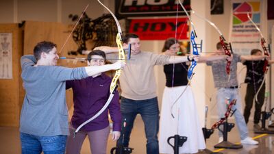 In der Strebel Bogensport AG in Sempach (6204, Kanton Luzern) üben mehrere Personen in einer Halle konzentriert das Bogenschiessen.