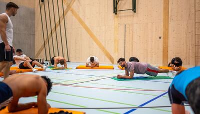 In Opfikon (8152, Kanton Zürich) trainieren Teilnehmende von Street Skills Glattbrugg in einer Turnhalle gemeinsam ihre Rumpfstabilität und Fitness bei einer angeleiteten Übungseinheit auf Gymnastikmatten.