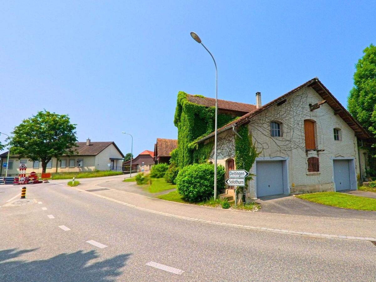 In Subingen (4553, Kanton Solothurn) führt die Straße an einem alten, mit Efeu bewachsenen Bauernhaus vorbei, während ein Wegweiser nach Dettingen zeigt.