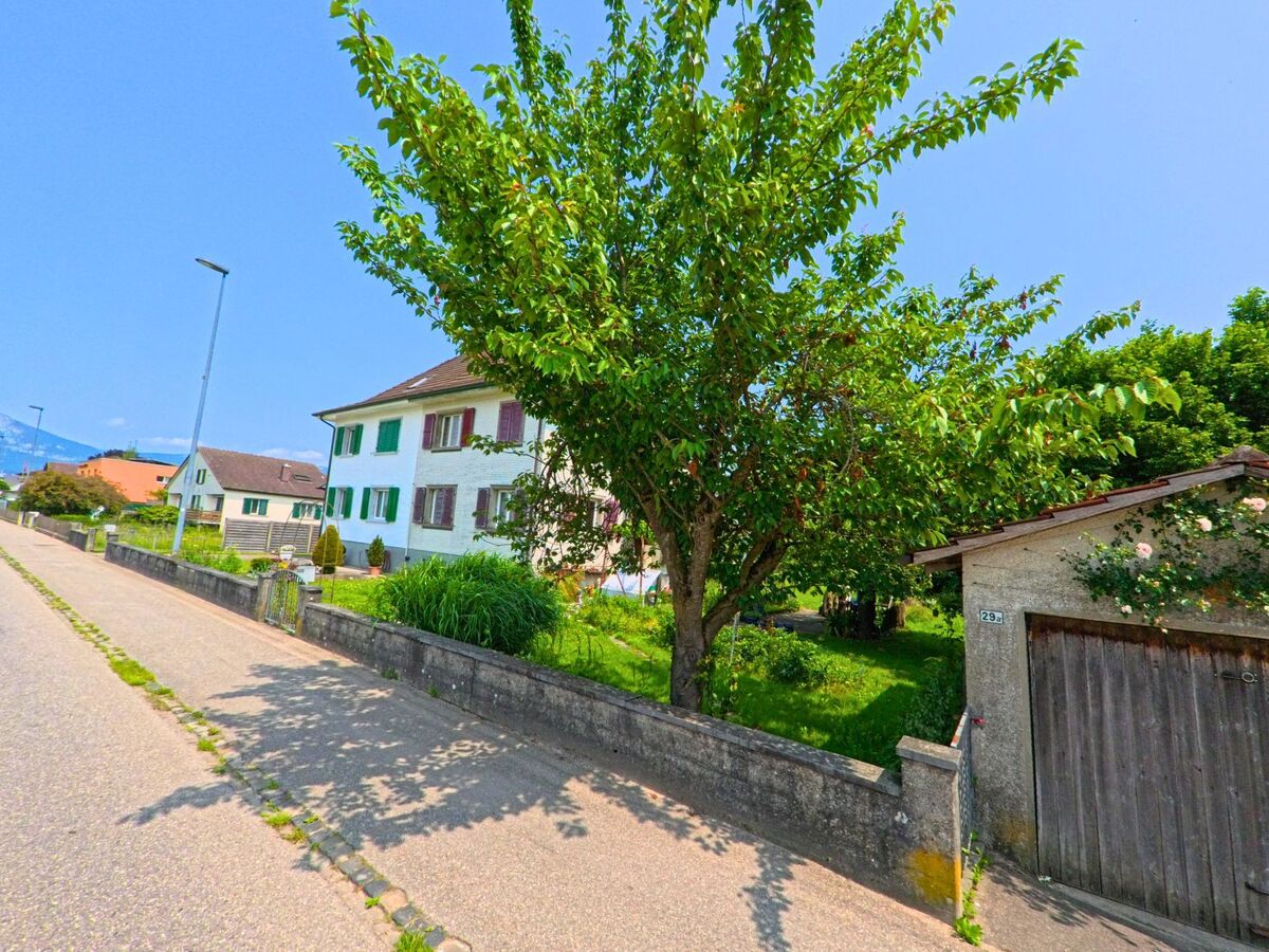 In Subingen (4553, Kanton Solothurn) steht ein mehrstöckiges Wohnhaus neben einer grünen Wiese und einem mit Rosen bewachsenen Garagentor.
