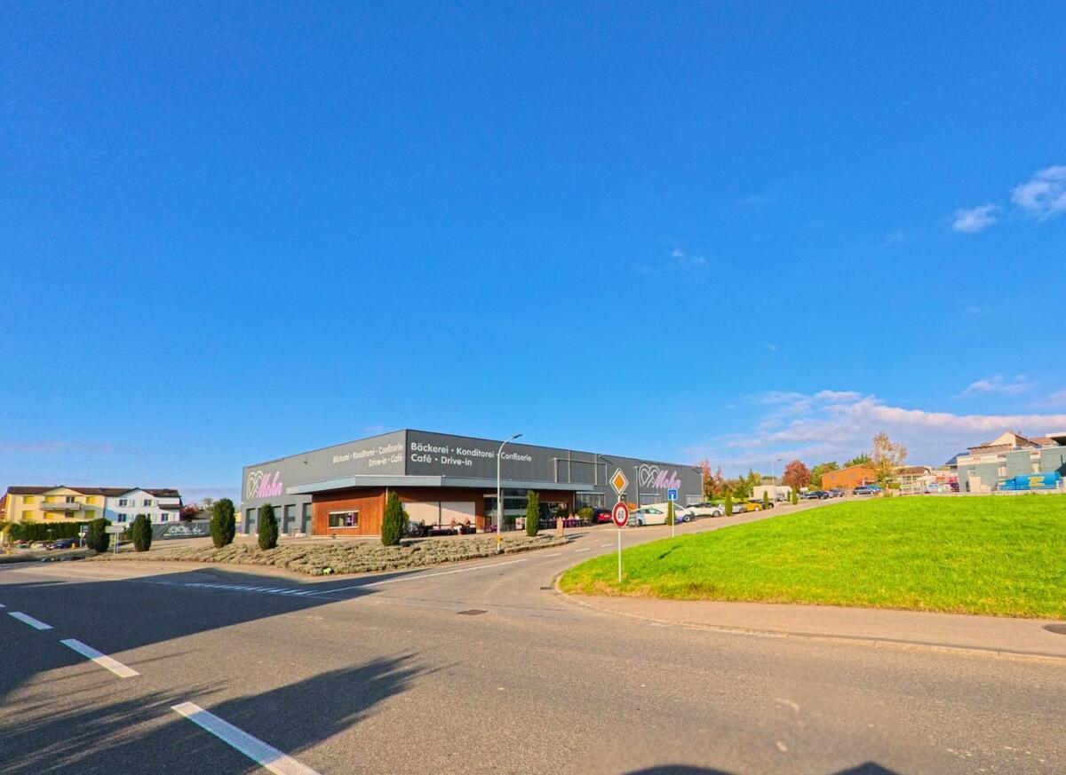An einer gut einsehbaren Kreuzung steht ein modernes Gewerbegebäude mit Aussenbereich in Sulgen (8583, Kanton Thurgau), umgeben von Strasse, Grünflächen und offener Bebauung.
