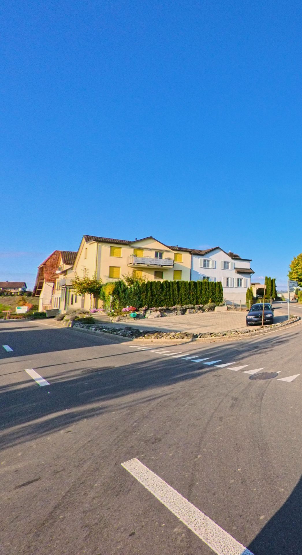 An einer leicht geschwungenen Strasse mit Kreuzungsbereich sind gepflegte Mehrfamilienhaeuser in Sulgen (8583, Kanton Thurgau) zu sehen, umgeben von Hecken und klar strukturierten Aussenraeumen.