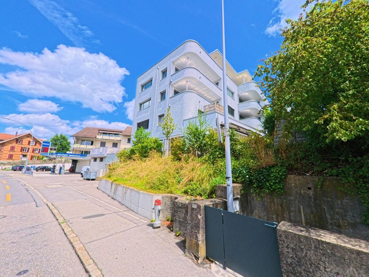 An einer leicht ansteigenden Strasse in Sursee (6210, Kanton Luzern) stehen moderne Wohnbauten mit geschwungenen Balkonen neben einer Tankstelle und traditionellen Haeusern.