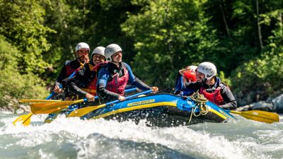 In Ilanz (7130, Kanton Graubuenden) paddelt eine Gruppe in Schutzkleidung und Helmen ueber spritziges Wasser, waehrend das Raft kraftvoll durch die Stromschnellen gleitet.