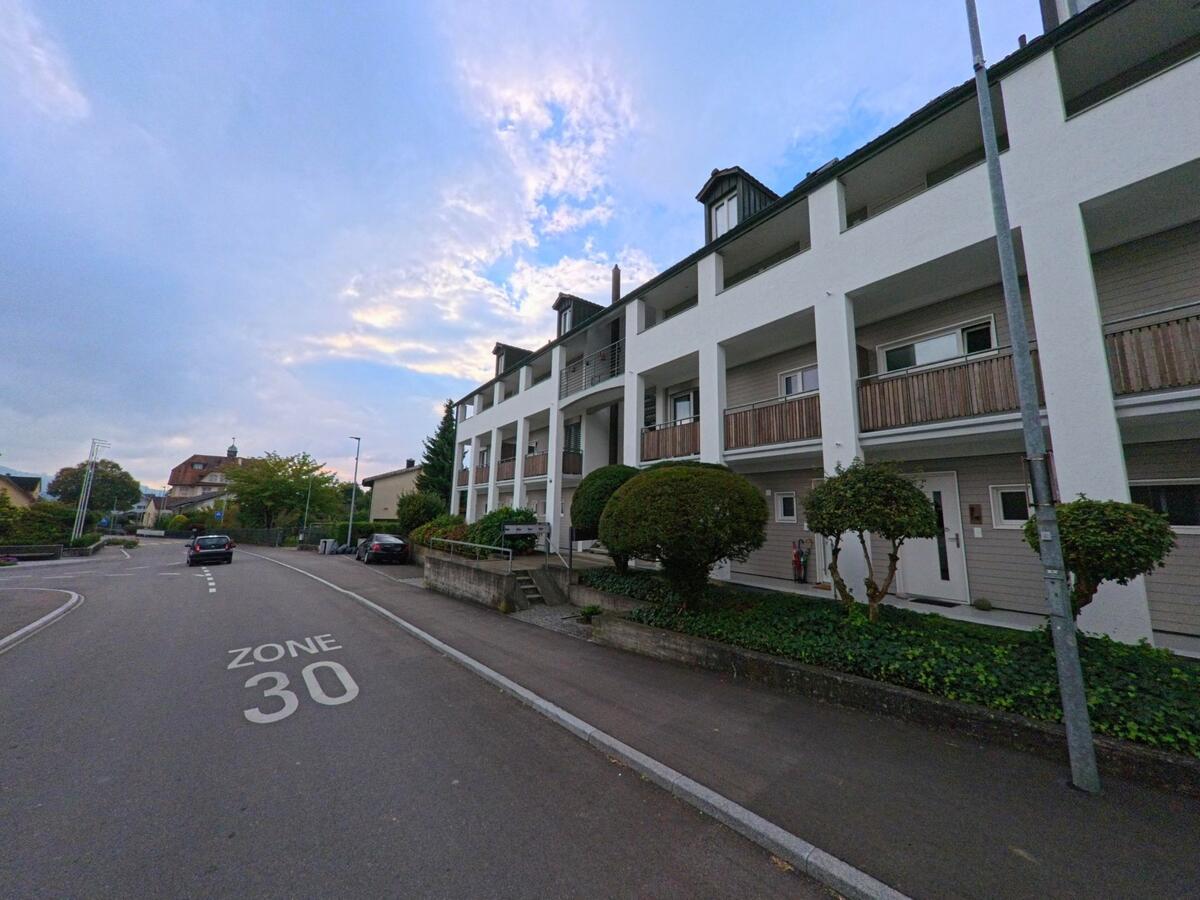 In Tägerig (5522, Kanton Aargau) verläuft eine Strasse durch eine verkehrsberuhigte Zone 30, gesäumt von modernen Wohnhäusern und gepflegten Sträuchern.