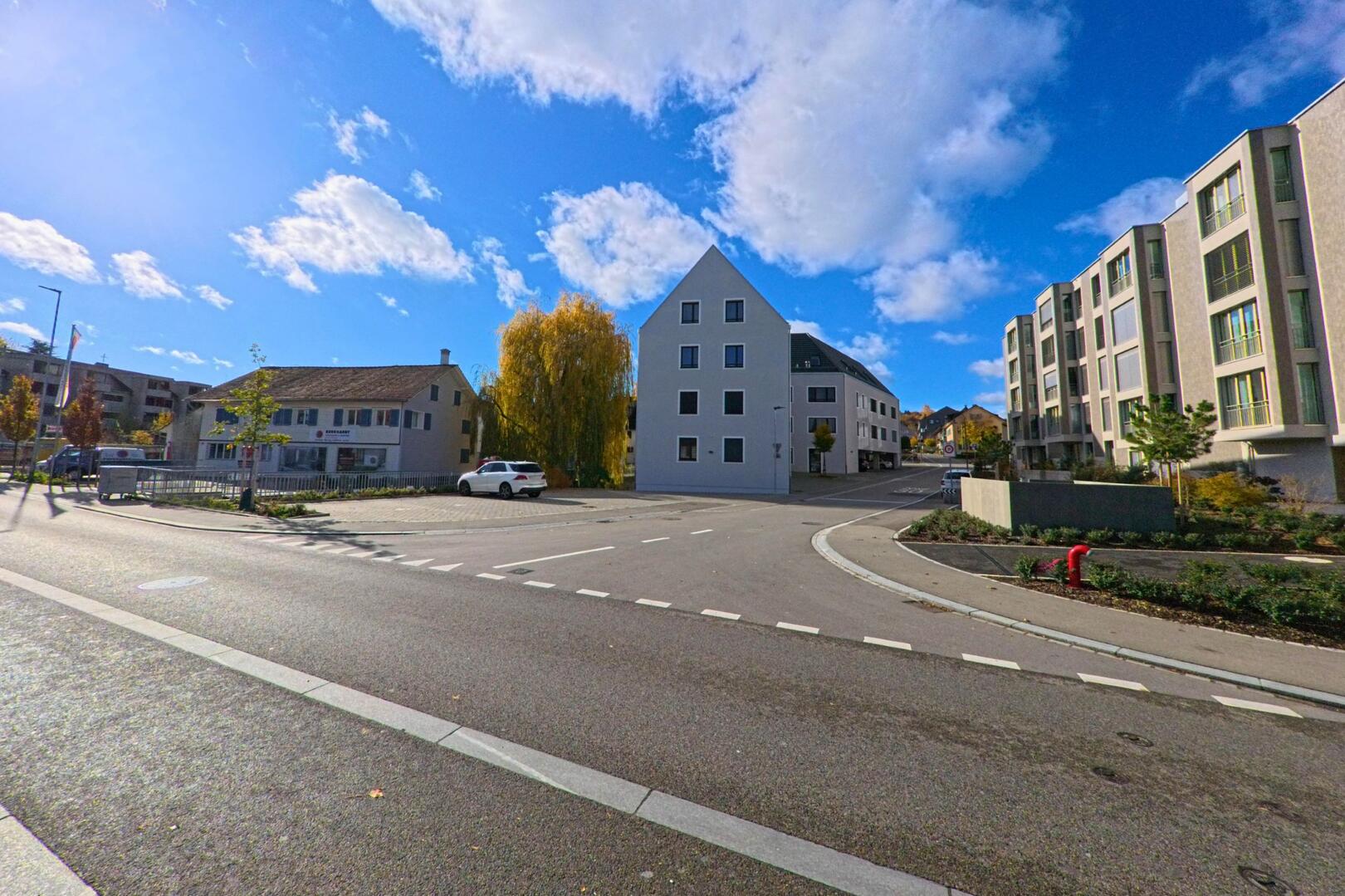An einer ruhigen Kreuzung mit modernen Wohnbauten zeigt sich ein Wohnquartier in Tägerwilen (8274, Kanton Thurgau) unter blauem Himmel mit herbstlichen Bäumen.