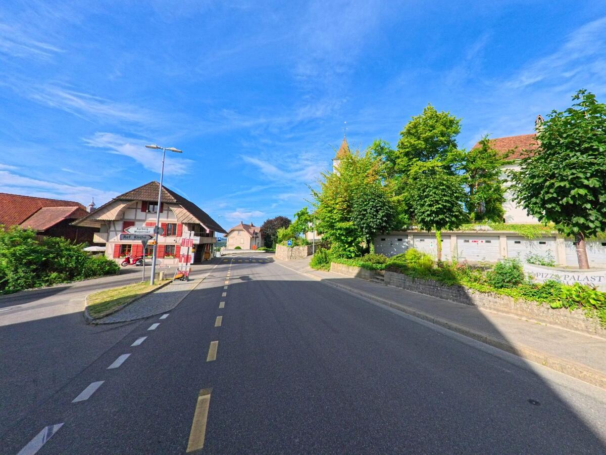 Im Zentrum von Täuffelen (2575, Kanton Bern) steht ein traditionelles Fachwerkhaus an einer Kreuzung mit Wegweisern und Briefkastenanlage vor einer Mauer.
