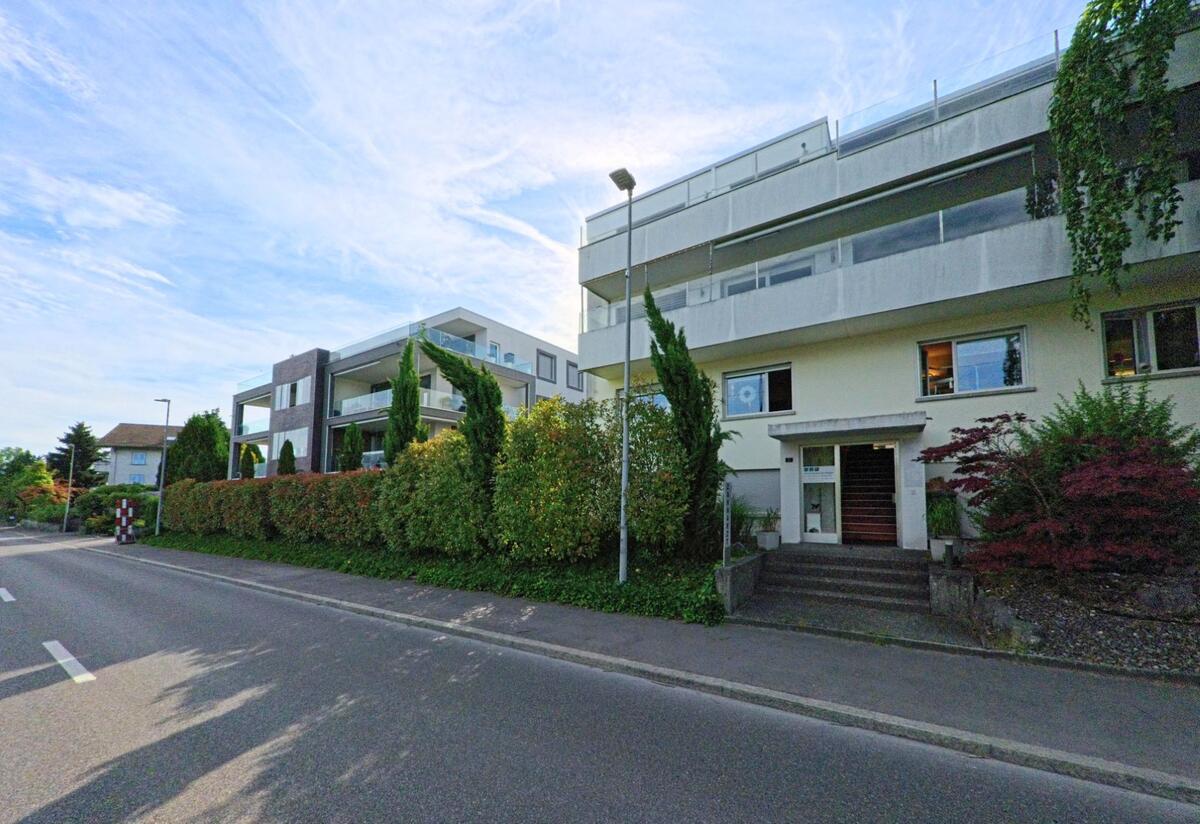 In Täuffelen (2575, Kanton Bern) reihen sich moderne Mehrfamilienhäuser mit Glasbalkonen und gepflegten Vorgärten entlang einer Hauptstrasse.
