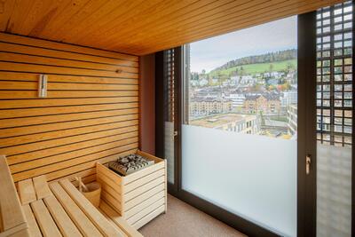 Im Tailormade Hotel LEO in St. Gallen (9000, Kanton St. Gallen) bietet eine moderne Sauna mit Holzverkleidung einen Ausblick auf die Stadt und die umliegenden Huegel.