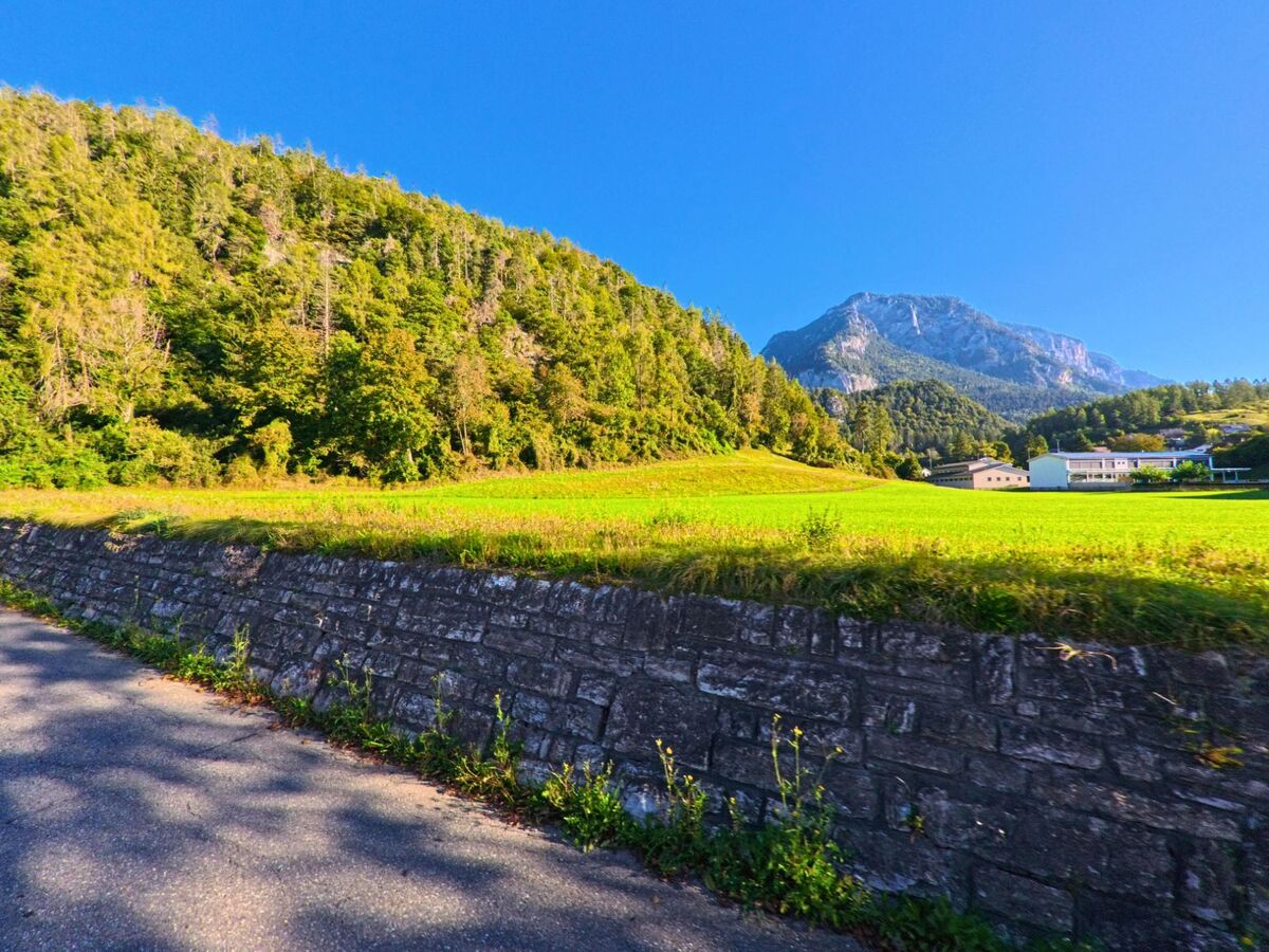 Ein traditionelles Wohnhaus in Tamins (7015, Kanton Graubuenden) mit Holzbalkon und angrenzender Scheune steht an einer leicht ansteigenden Strasse.