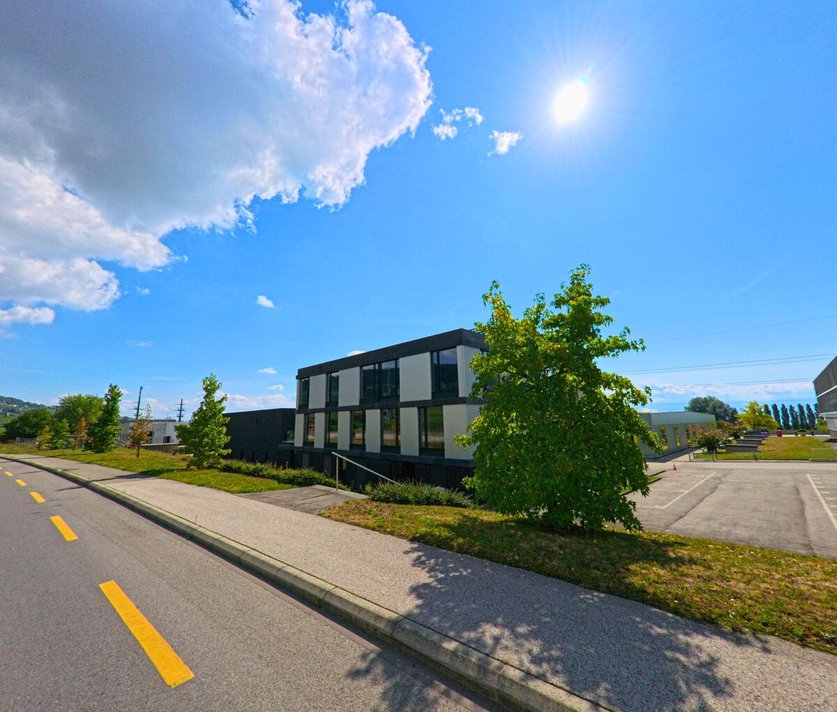 Ein modernes Gewerbegebaeude mit grossen Fenstern steht am Strassenrand in Tartegnin (1180, Kanton Waadt).