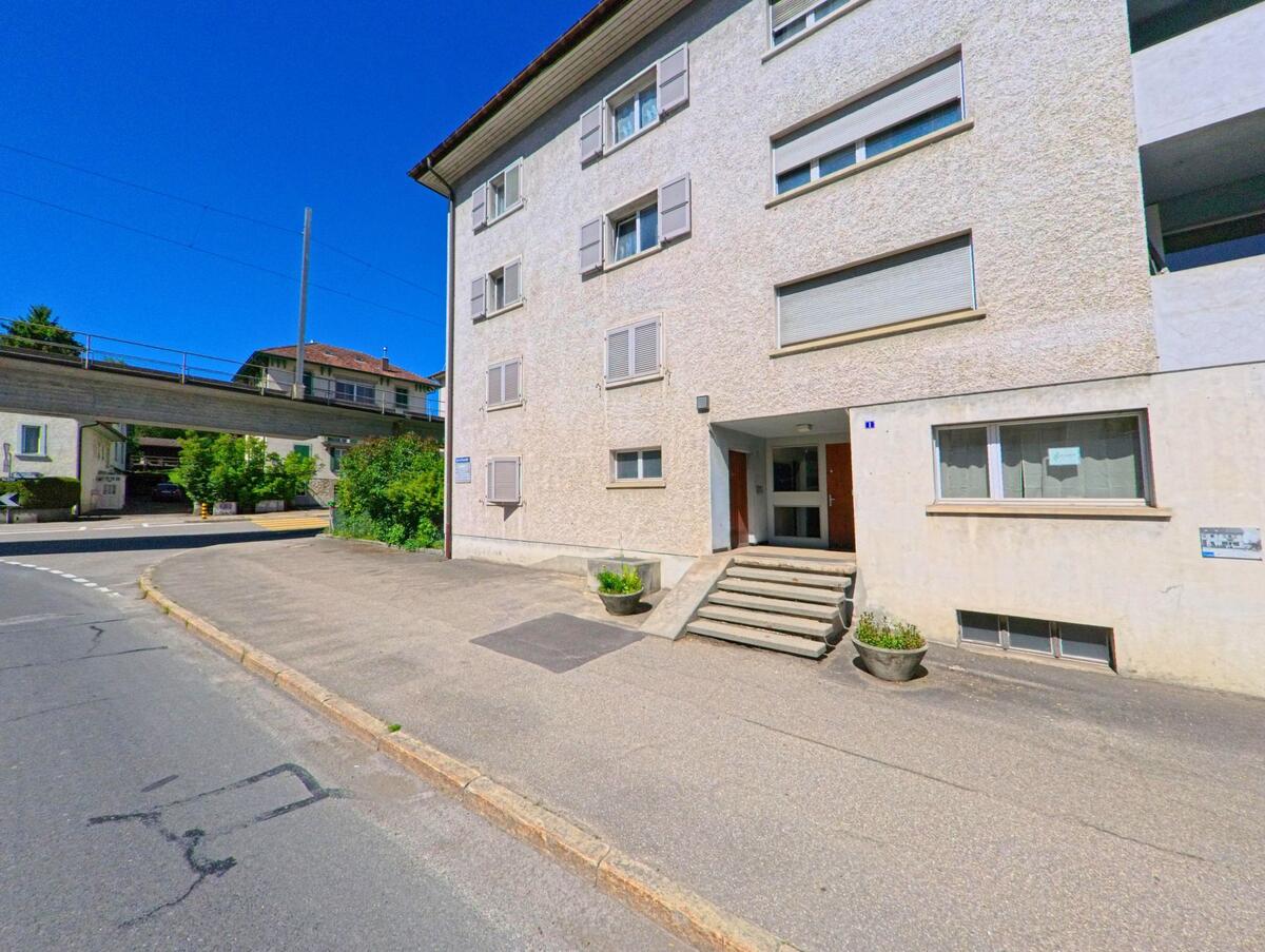 In Tavannes (2710, Kanton Bern) ist ein Mehrfamilienhaus entlang der Strasse zu sehen, mit einer erhöhten Brücke, die darüber führt.