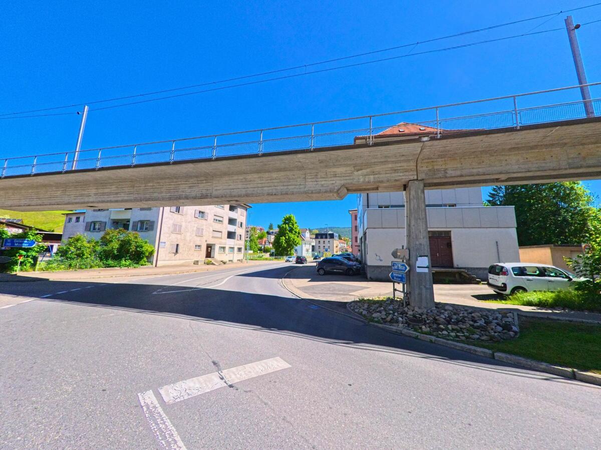 In Tavannes (2710, Kanton Bern) führt eine Strasse unter einer erhöhten Brücke hindurch, die den Blick auf angrenzende Gebäude und die klare Himmelssicht freigibt.