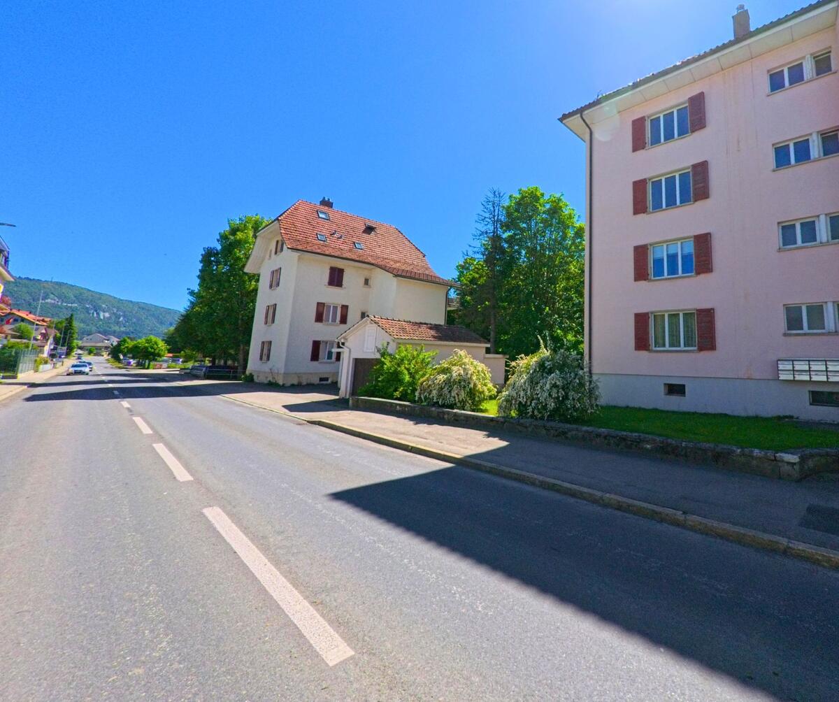 In Tavannes (2710, Kanton Bern) führt die Strasse an einem modernen, mehrstöckigen Gebäude entlang, das von Bäumen und einer grünen Wiese umgeben ist.