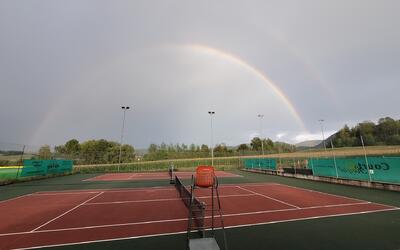 Die Tennisplätze des TC Laufen in Laufen (4242, Kanton Basel-Landschaft) liegen unter einem Regenbogen und sind von Feldern, Bäumen und einer ländlichen Landschaft umgeben.