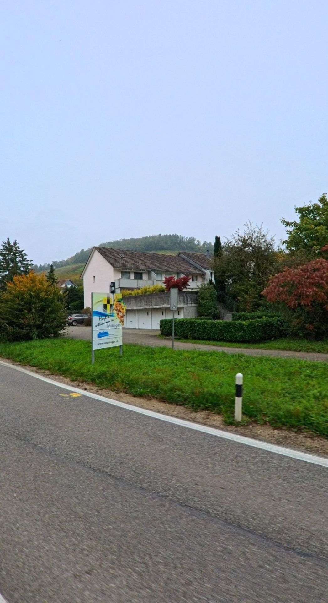 Entlang der Ausfahrt aus Tegerfelden (5306, Kanton Aargau) steht ein Wohnhaus vor herbstlicher Vegetation, waehrend ein Wegweiser auf die nahegelegene Gemeinde Doettingen hinweist.