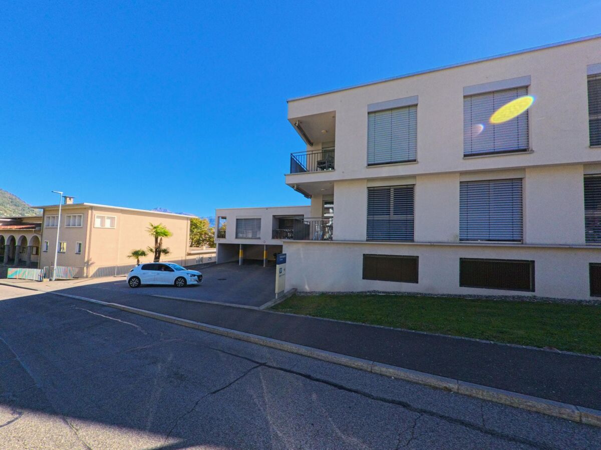 Ein modernes Wohngebäude mit grossen Fenstern und einer Zufahrt zu Tiefgaragen steht in Tenero-Contra (6598, Kanton Tessin) an einer ruhigen Nebenstrasse.