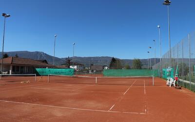 Mehrere Sandtennisplätze liegen im Freien mit Blick auf Berge und Gebäude in Derendingen (4552, Kanton Solothurn) und zeigen eine Sportanlage.