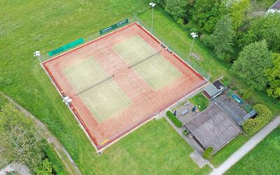 In Fraubrunnen (3312, Kanton Bern) sind zwei Sandtennisplaetze von oben sichtbar, umgeben von Gruenflaechen und einem Clubhaus.