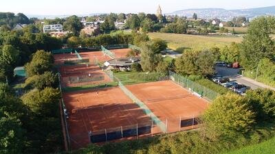 In Kilchberg (8802, Kanton Zuerich) zeigt die Aufnahme mehrere rote Sandplaetze des Tennisclubs, die zwischen Baeumen und nahe der umliegenden Wohnhaeuser liegen.