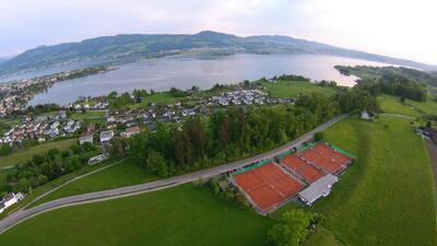 Die Tennisplätze des Tennisclubs Lenggis in Rapperswil-Jona (8645, Kanton St. Gallen) liegen in einer grünen Landschaft mit Blick auf den See und die umliegenden Hügel.