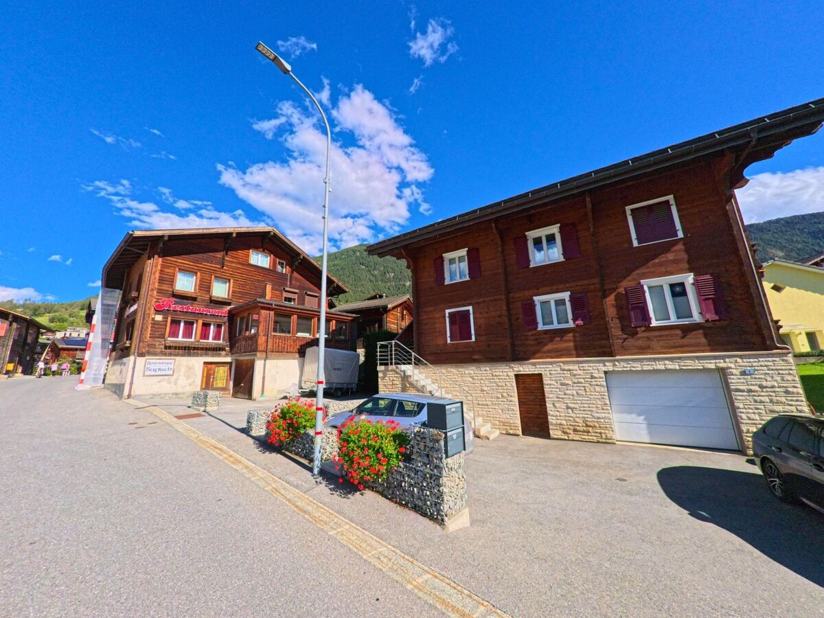 Traditionelle Holzhäuser mit Restaurant in Termen (3912, Kanton Wallis) stehen an einer Strasse, geschmückt mit Blumenkästen.