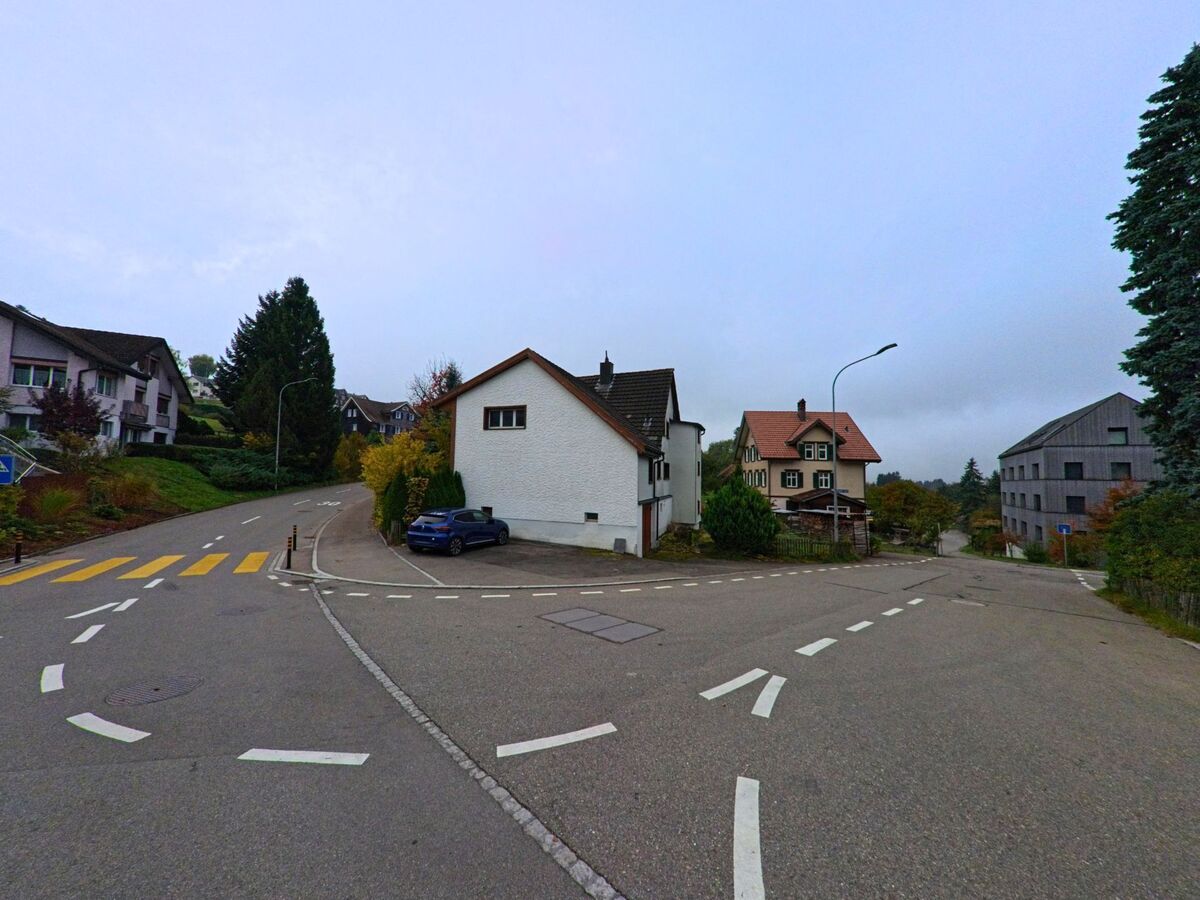 An einer weitlaeufigen Abzweigung in Teufen (9012, Kanton Appenzell Ausserrhoden) stehen mehrere Wohnhaeuser zwischen herbstlichen Baumen und leicht ansteigenden Strassen.