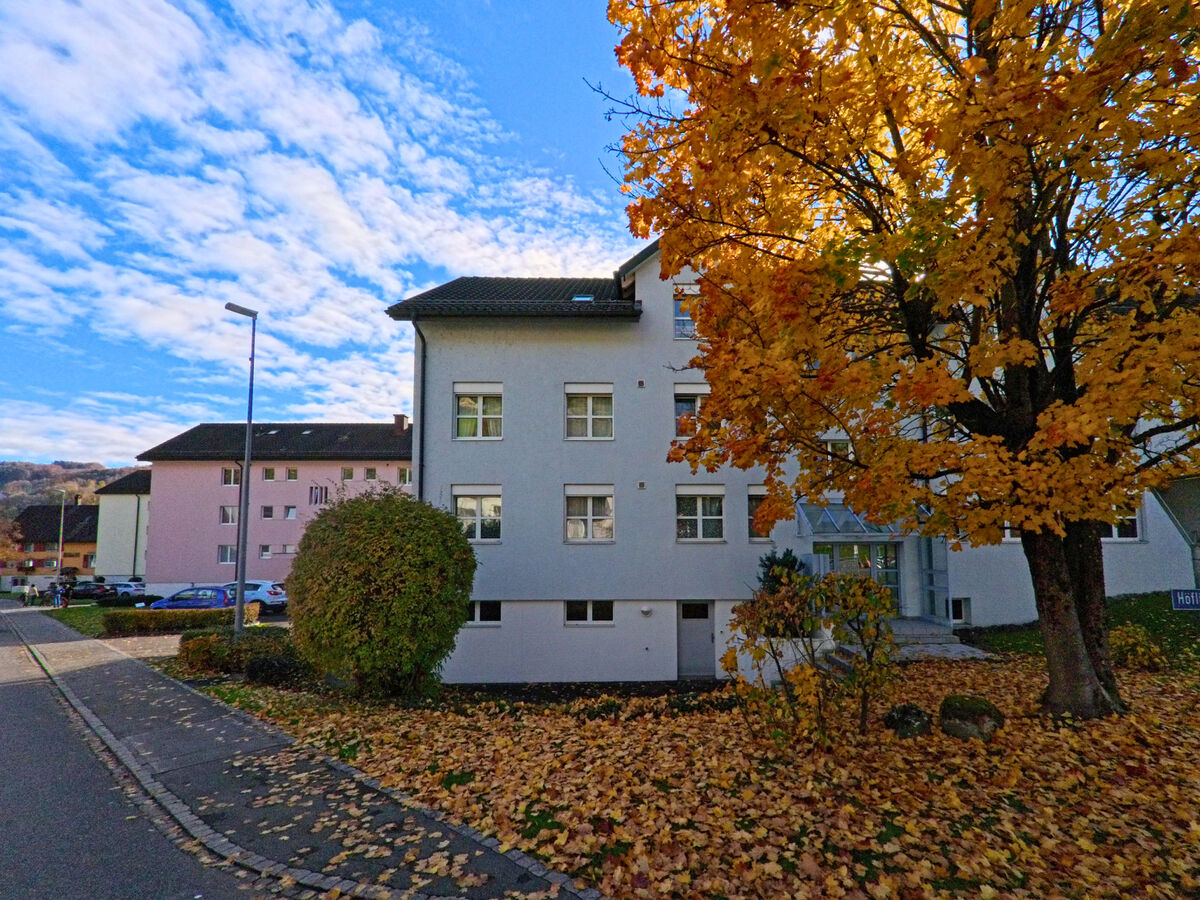 Ein Mehrfamilienhaus mit Vorgarten liegt an einer Nebenstrasse in Thal (9425, Kanton St. Gallen) im Herbst.
