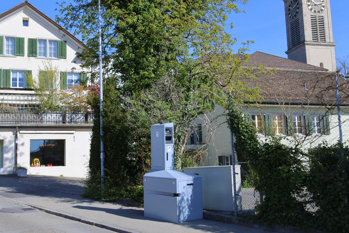 Vor einem Wohnhaus mit gruenen Fensterlaeden steht ein Sammelbehaelter an einer ruhigen Strasse in Thalwil (8800, Kanton Zürich).