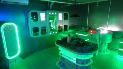 Im The Factory Escape Game in Courtételle (2852, Kanton Jura) befindet sich ein futuristisch gestalteter Raum mit grüner Beleuchtung, Kontrollpulten und 3D-Modellen.