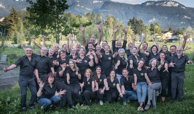 Die Theatergruppe Rhybrugg steht in Diepoldsau (9444, Kanton St. Gallen) gemeinsam im Freien und laechelt vor bergiger Landschaft in die Kamera.