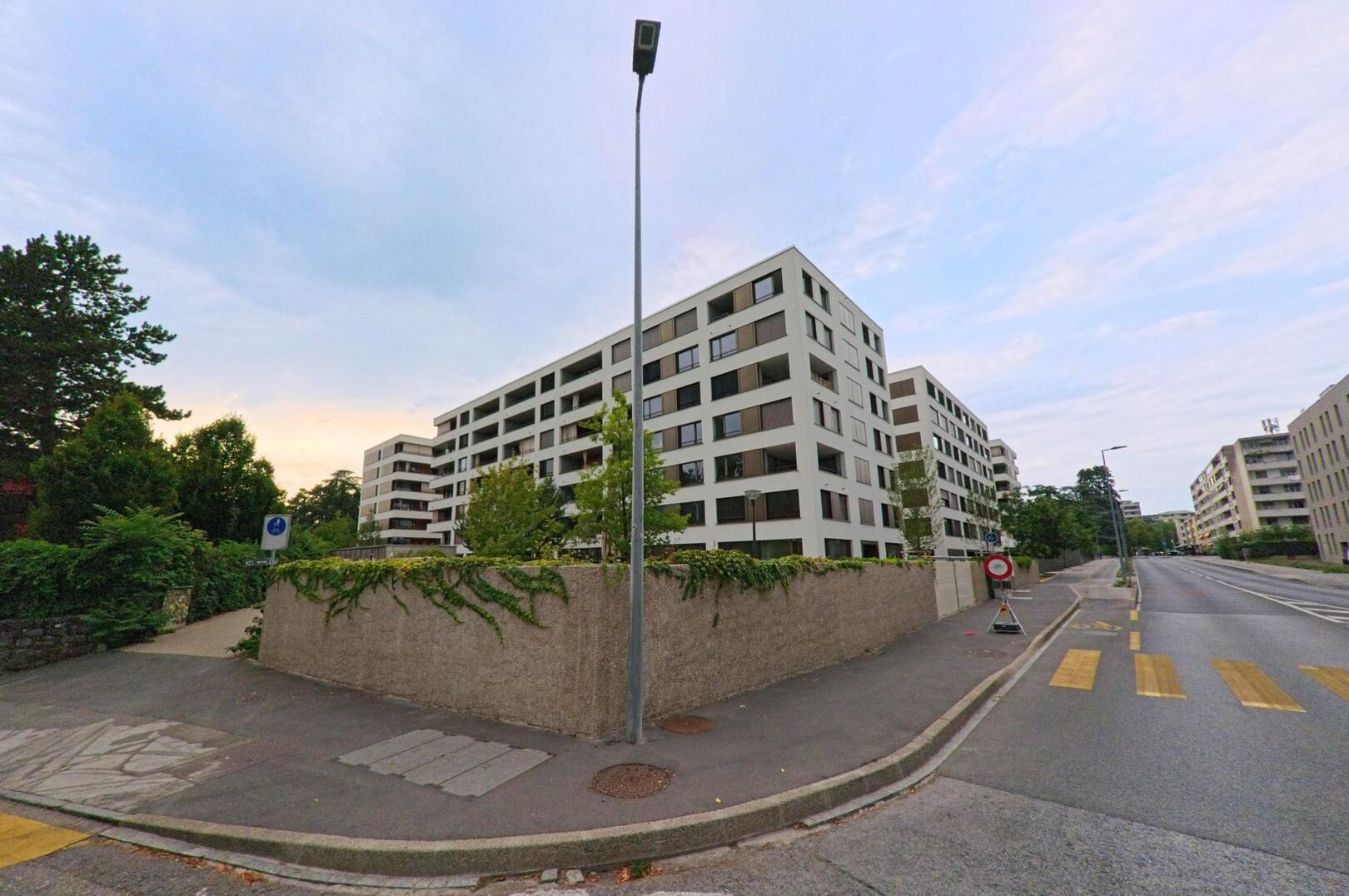 Mehrere moderne Wohnblocks mit Balkonen stehen in Thonex (1226, Kanton Genf) entlang einer breiten Strasse mit Fussgaengerstreifen.