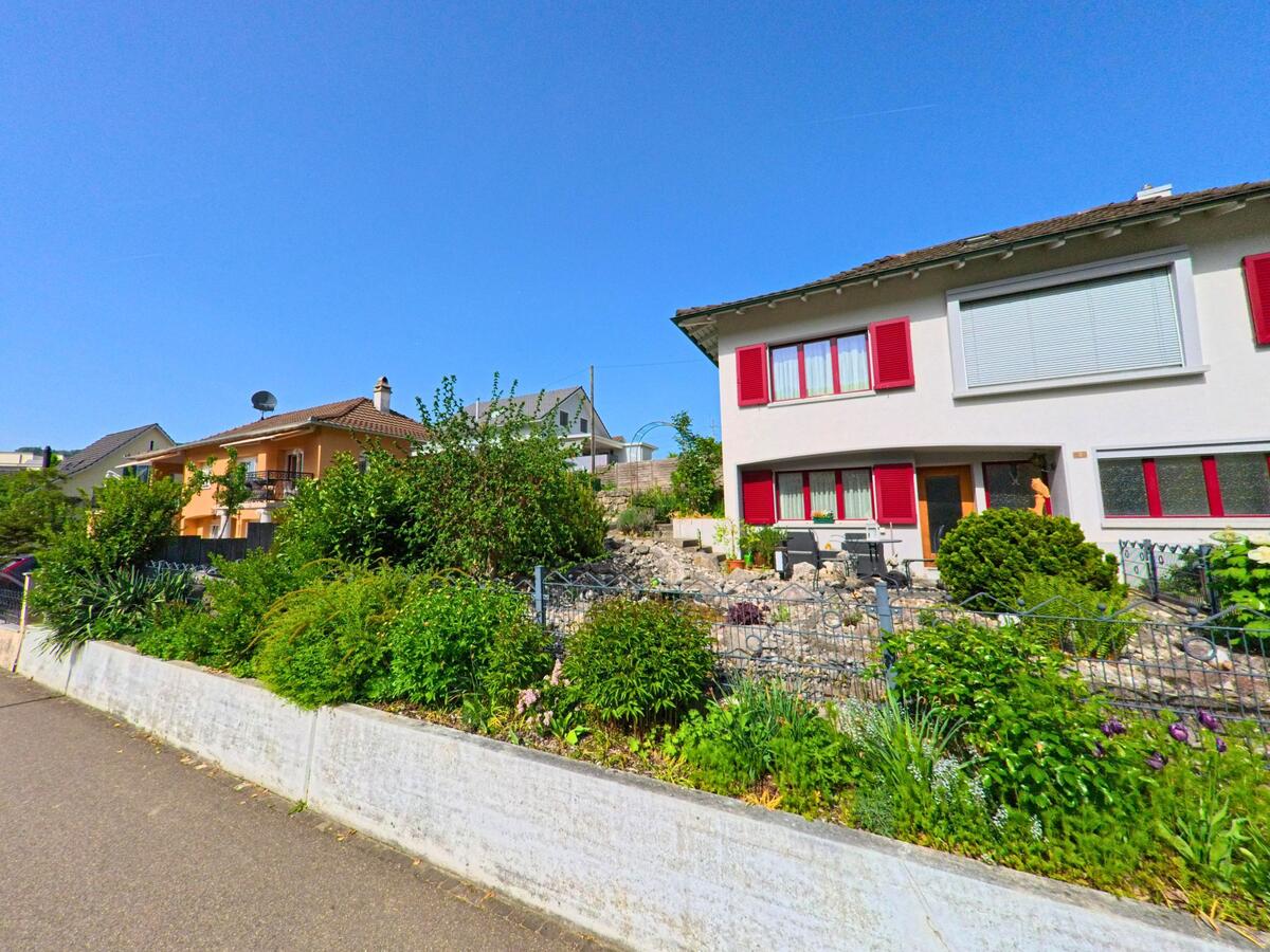 In Thürnen (4441, Kanton Baselland) reihen sich moderne Einfamilienhaeuser mit gepflegten Vorgärten und bunten Fensterlaeden entlang eines ruhigen Gehwegs.
