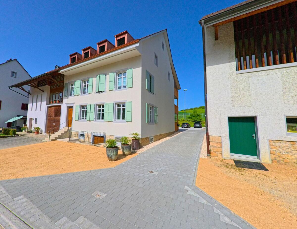 In Thürnen (4441, Kanton Baselland) steht ein frisch renoviertes Wohnhaus mit mintfarbenen Fensterlaeden und breiter Steintreppe neben einem gepflasterten Zufahrtsweg.